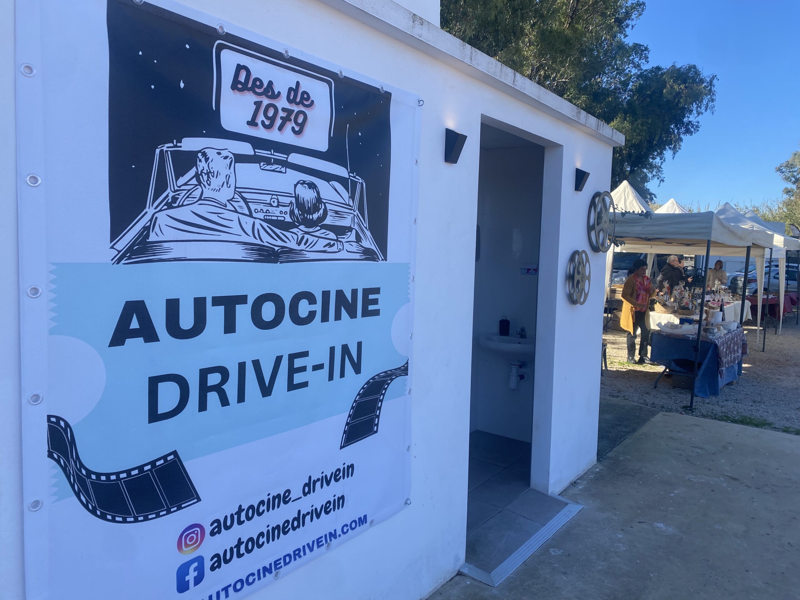 Sign for the Auto-cine with market stands in the back.